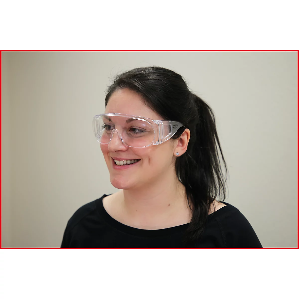 Eine lächelnde Frau mit Brille. Sie trägt eine Schutzbrille. Schwarzes Oberteil, Haare zum Pferdeschwanz gebunden.